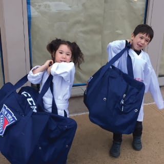 Two Children Posing with Hockey Bags At New York Rangers Learn To Play Event