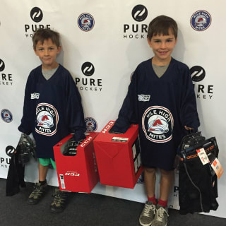 Two Youn Children With Hockey Equipment Posing For Picture In Front Of Pure Hockey Logo Backdrop