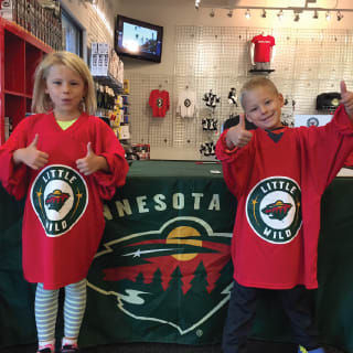 Two Childre In Minnesota Wild Learn To Play Jerseys Posing with Hockey Gloves At Minnesota Wild Learn To Play Event