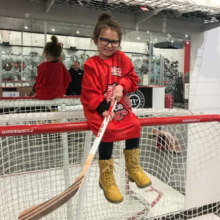 Young Child Playfully Sitting on Top of Hockey Goal with Hockey Stick