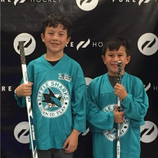 Two Young Kids In San Jose Sharks Learn To Play Jerseys Holidng Hockey Sticks And Smiling At Camera